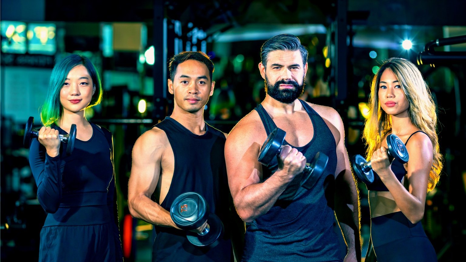 People at gym holding dumbbells preparing to perform bicep workouts.